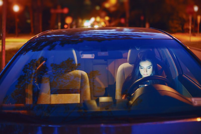 Woman sitting alone in her car at night using cell phone