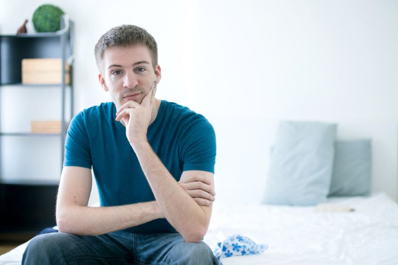 Man sitting curiously on his mattress at home